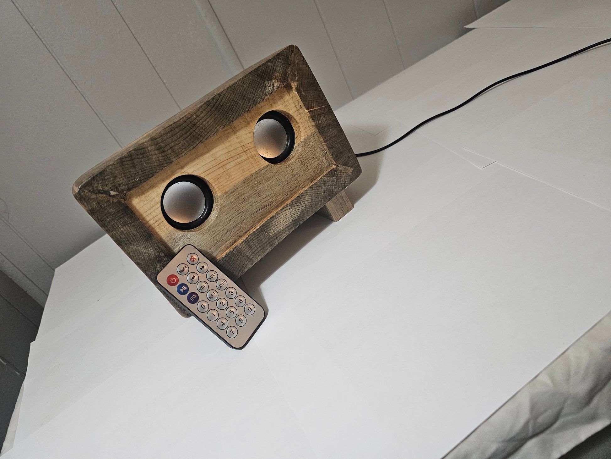 Wooden radio speaker and a remote control on a white surface.